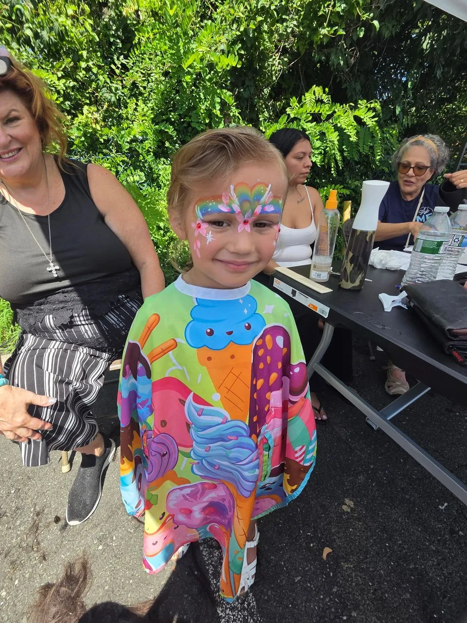 Smiling child with rainbow face painting after a free haircut at a Salon DP Lorana community event
